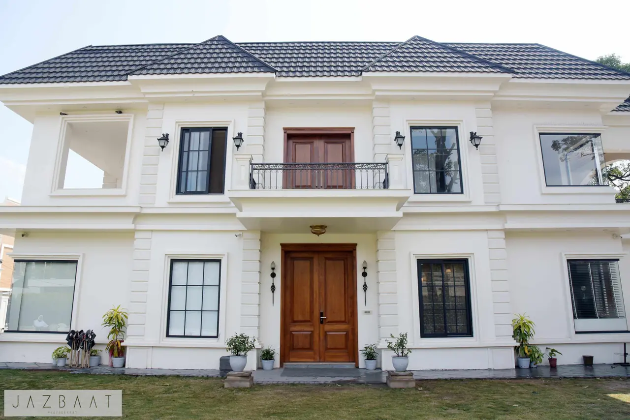 Archmere, a residence by Ajooni Jasleen Architects: symmetrical white facade with a charcoal tiled roof, timber double doors and a wrought-iron balcony