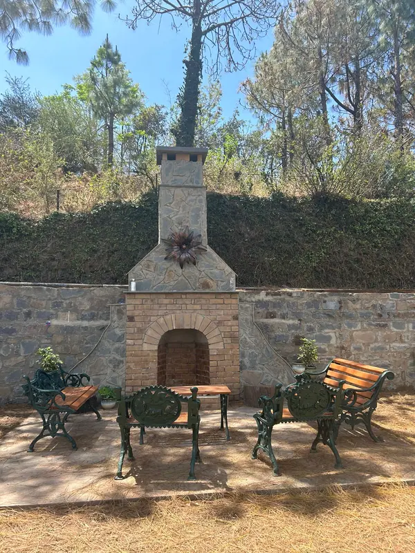 Kasauli Cottage: stone outdoor fireplace and garden seating against a terraced hillside with pine trees